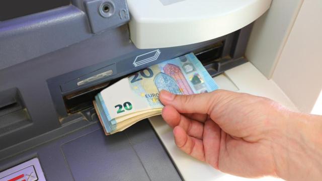 Una mano retirando billetes de 20 euros en un cajero.