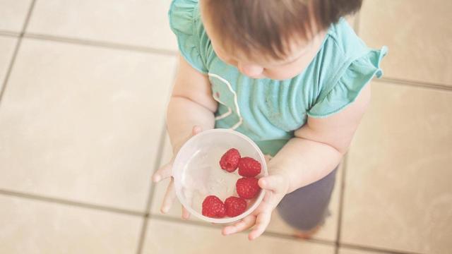 Un bebé con un vaso de frambuesas